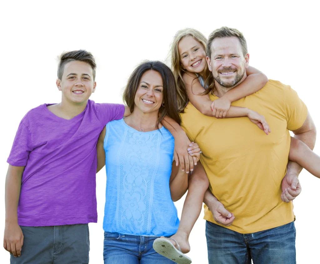 A family of four poses outdoors. Two children stand next to a woman wearing a blue top, and a man supports a girl on his back.